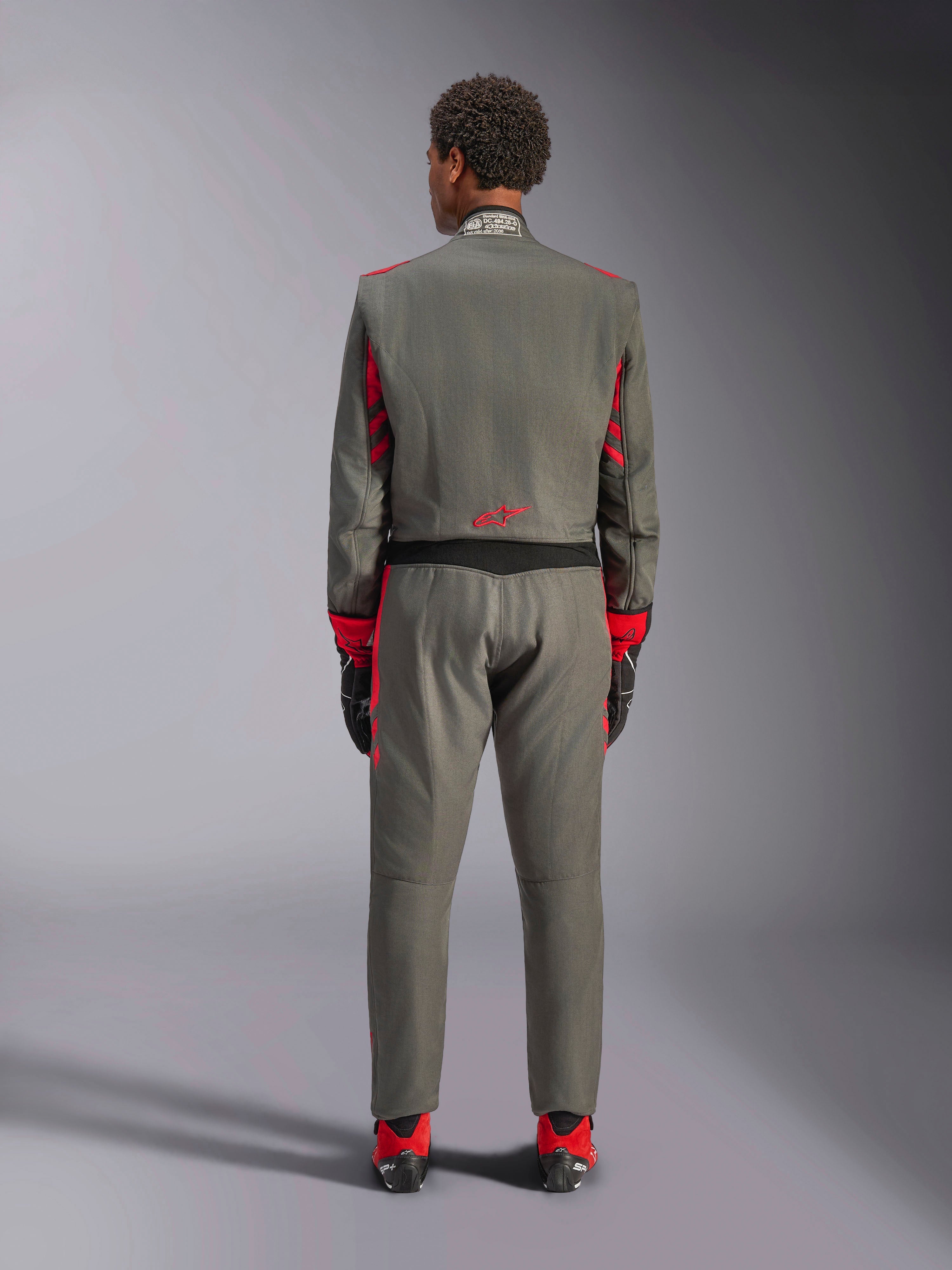 Vue arrière d'un mannequin portant la combinaison Alpinestars GP Race V3 en Anthracite Red, combinaison de course automobile professionnelle avec des accents rouges sur les manches et les jambes, associée à des bottines de course rouges et des gants noirs, équipement technique de sport automobile présenté en studio.