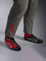 Combinaison Alpinestars GP Race V3 FIA, combinaison de course anthracite et rouge, gros plan sur le bas des jambes avec logo étoile rouge brodé, accompagnée de bottines de course rouges et noires, équipement automobile professionnel conçu pour la protection et le confort du pilote