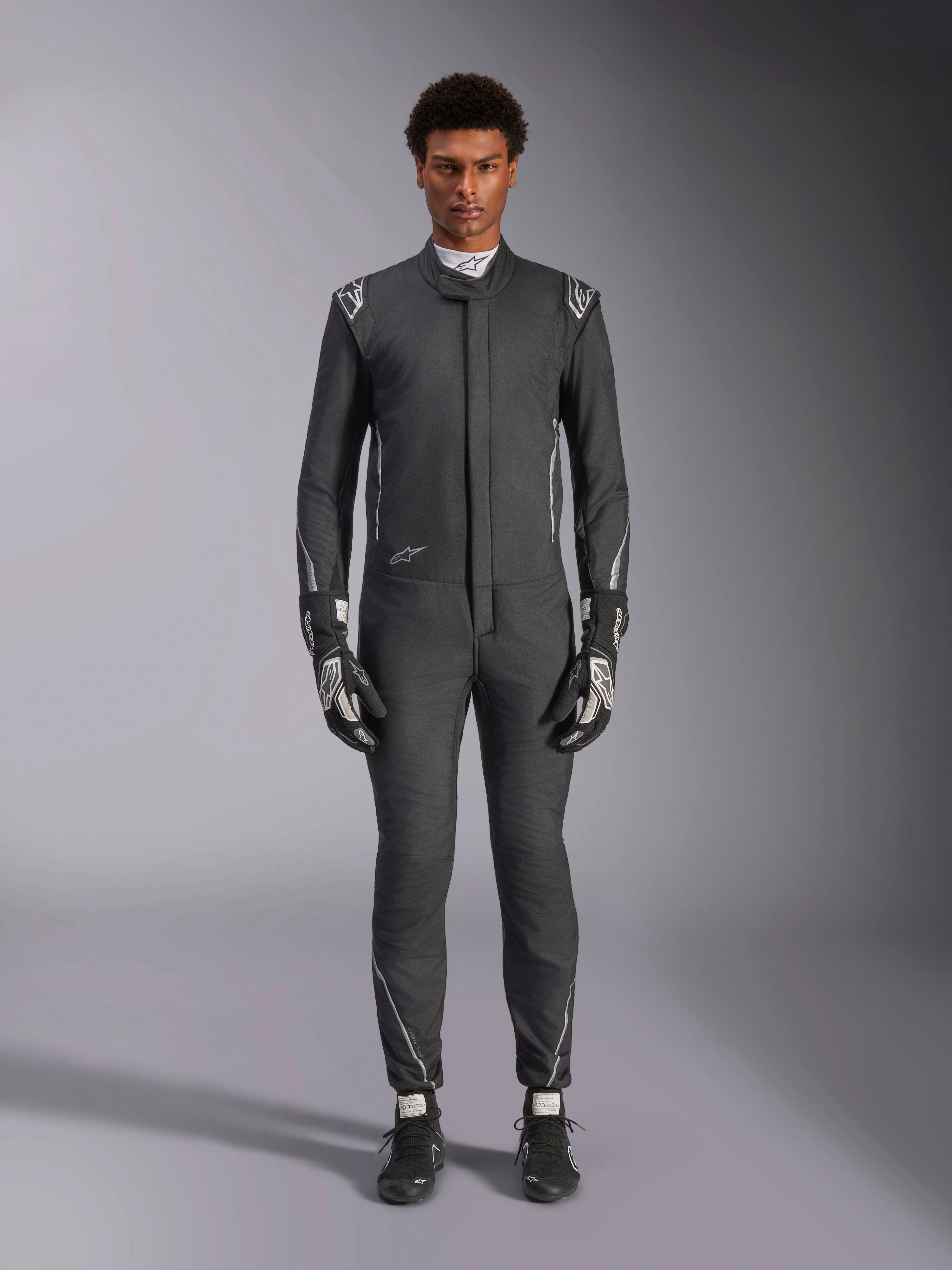 Combinaison Alpinestars Hypertech V3, combinaison de course automobile professionnelle, Noir et Dark Shadow, portée par un mannequin avec gants et chaussures de course assortis, coupe athlétique slim avec accents argentés et logos, équipement de sport automobile haute performance