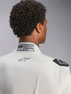 Combinaison Alpinestars Hypertech V3, blanc, vue détaillée du col arrière et de l'épaule, présentant l'étiquette de certification FIA 8856-2018, le logo Alpinestars gris imprimé et la poignée d'extraction noire, équipement de course professionnel
