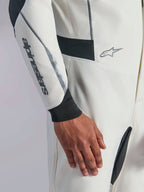 Combinaison Alpinestars Hypertech V3, gros plan d'une combinaison de course automobile blanche avec des accents noirs et argentés, logo Alpinestars sur l'avant-bras, poignet en tricot noir et panneaux extensibles sombres pour la mobilité, vêtement de sport automobile professionnel.