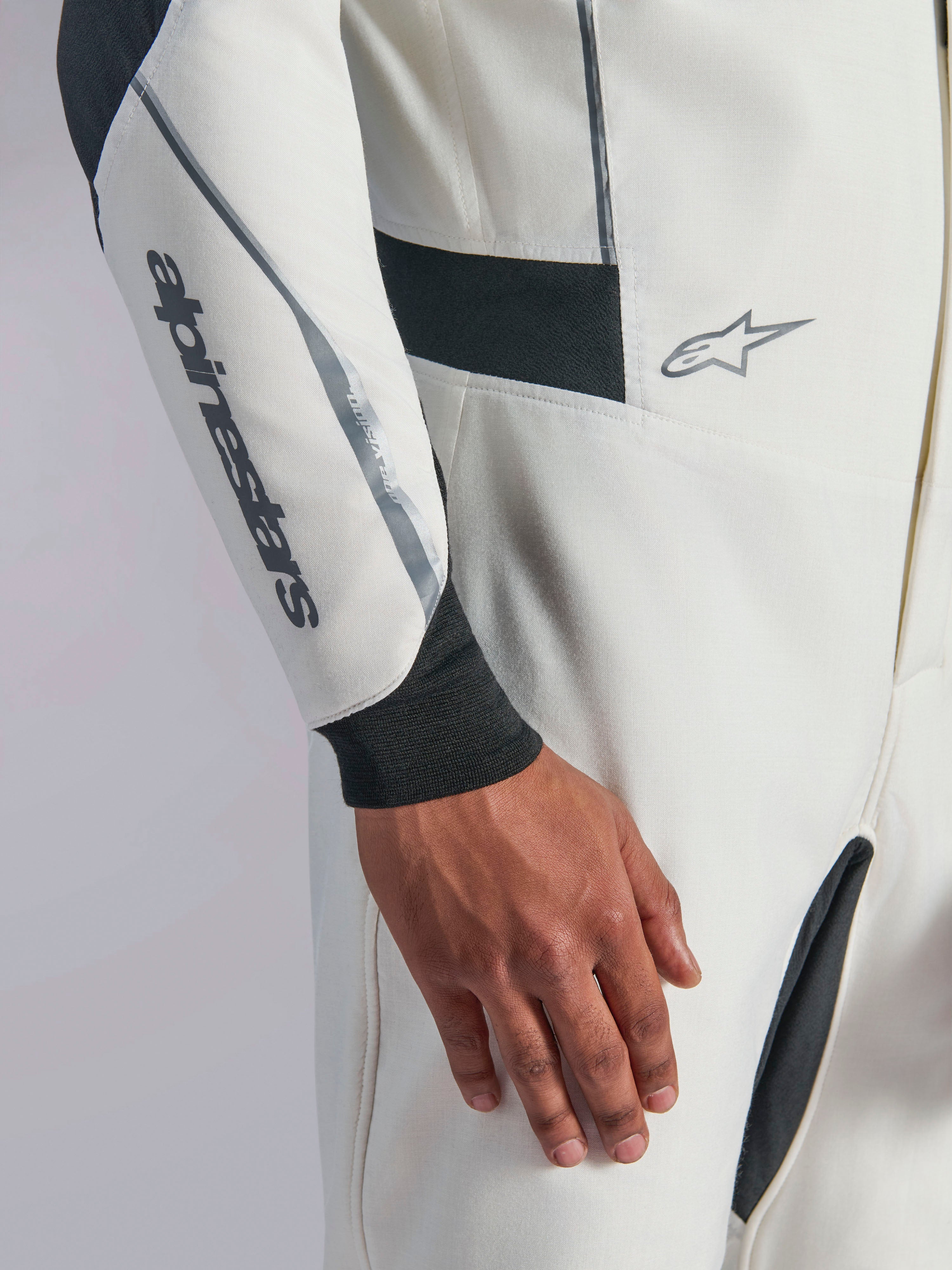 Combinaison Alpinestars Hypertech V3, gros plan d'une combinaison de course automobile blanche avec des accents noirs et argentés, logo Alpinestars sur l'avant-bras, poignet en tricot noir et panneaux extensibles sombres pour la mobilité, vêtement de sport automobile professionnel.