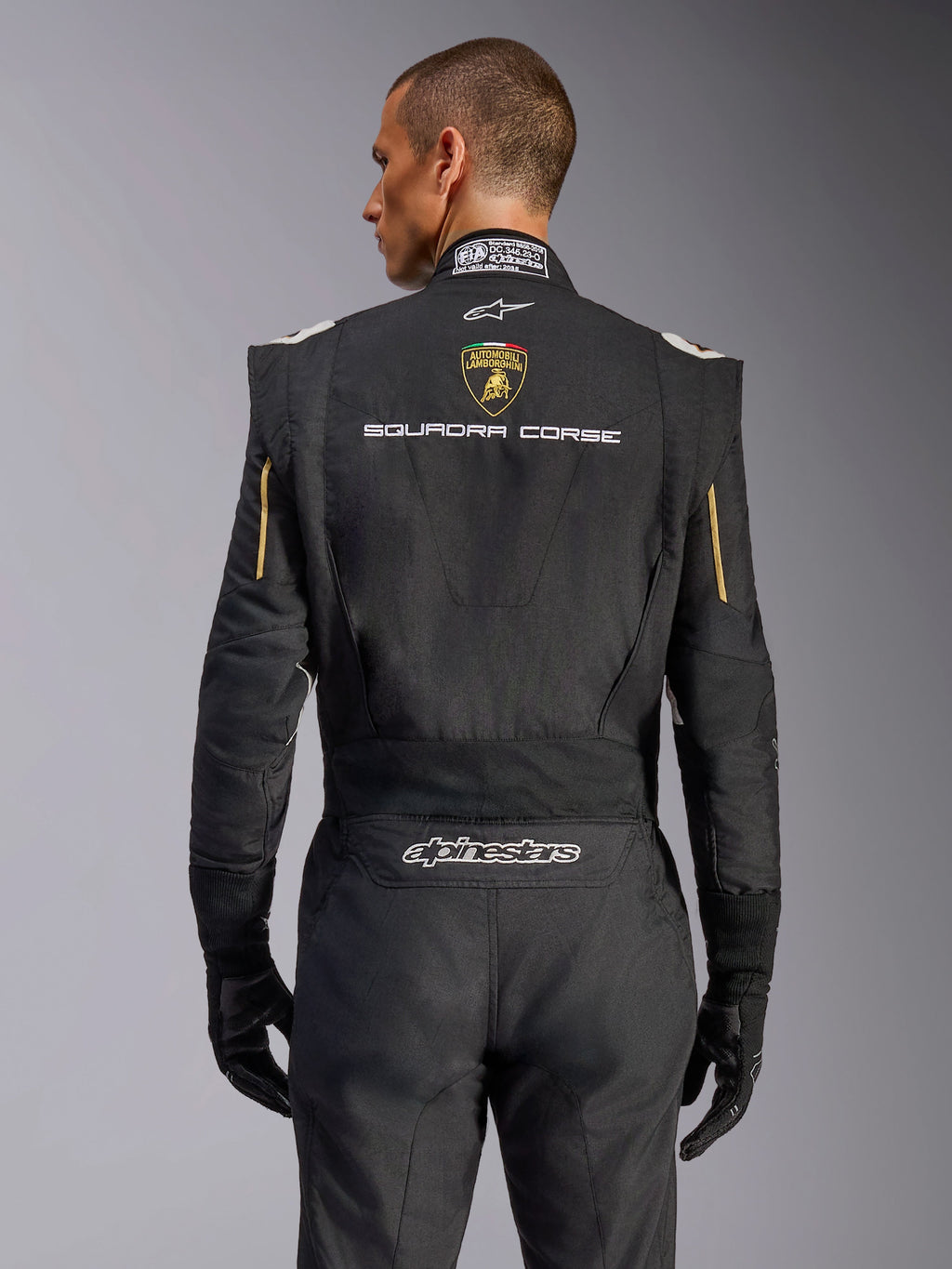 Vue arrière de la combinaison Alpinestars GP Tech V4 Édition Limitée Lamborghini, noire avec accents dorés, présentant l'écusson Automobili Lamborghini et le texte « SQUADRA CORSE » dans le dos, combinaison de course professionnelle certifiée FIA pour la compétition automobile