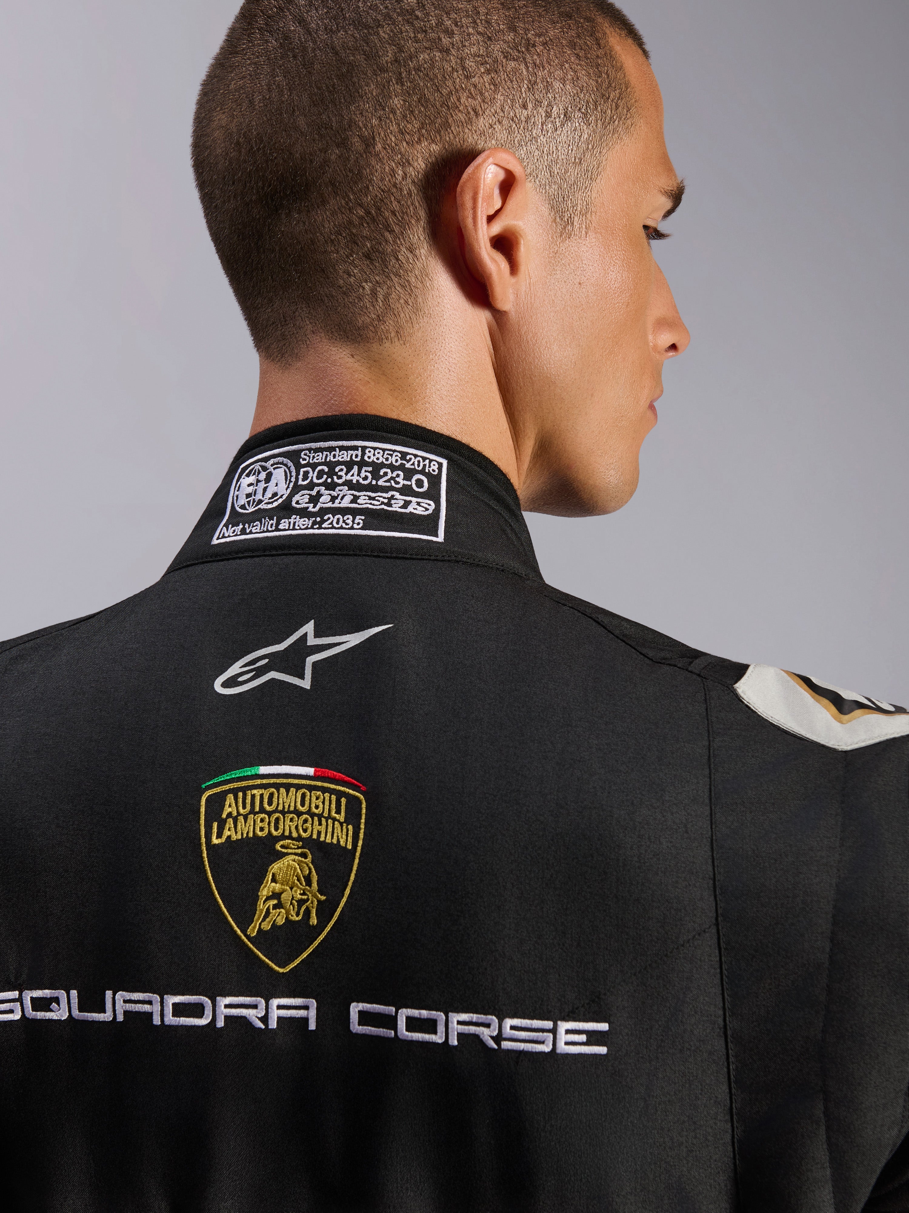 Combinaison Alpinestars Édition Limitée Lamborghini GP Tech V4 FIA, gros plan sur le haut du dos et le col, combinaison noire présentant l'écusson Automobili Lamborghini et la broderie Squadra Corse, logo Alpinestars et étiquette de certification FIA 8856-2018 sur l'encolure.