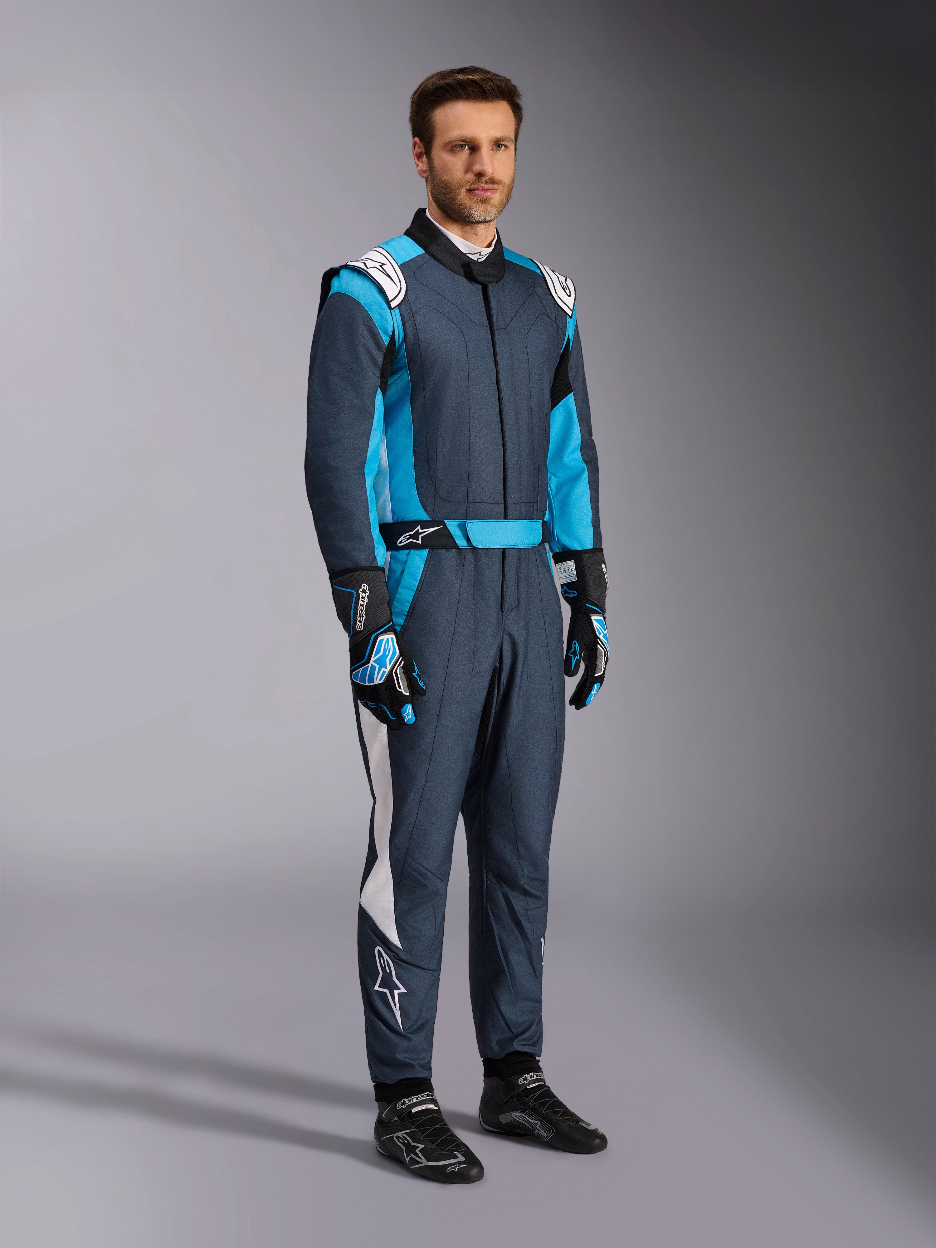 Alpinestars GP Pro Comp V2 FIA Suit, professional auto racing gear in Asphalt and Cyan, worn by a man.
