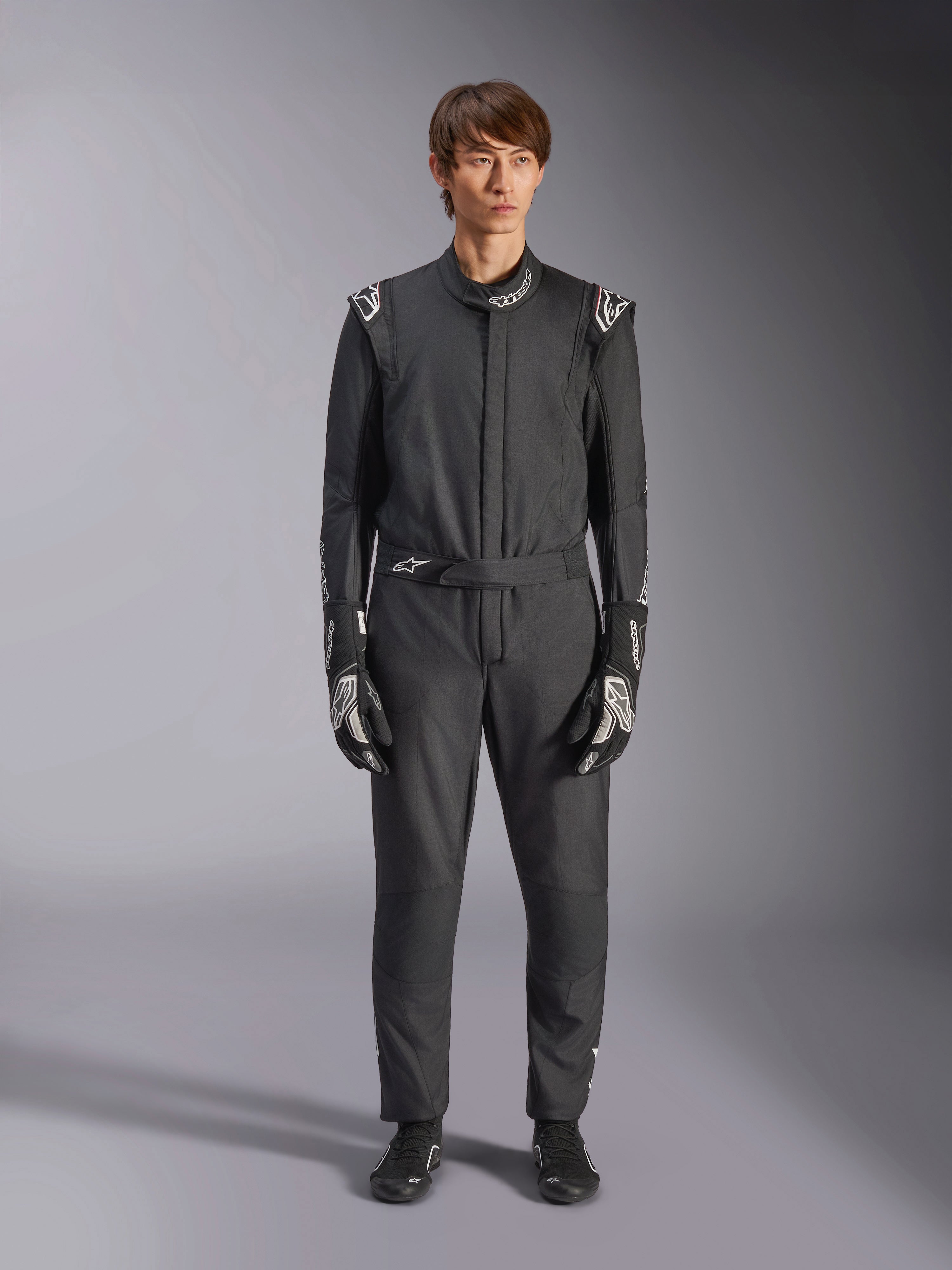 Combinaison Alpinestars GP Tech V4, noir et blanc, combinaison de course automobile professionnelle une pièce, portée avec des gants et des bottines de course assortis noirs et blancs, avec logos Alpinestars blancs sur les épaules et le col, coupe athlétique élégante pour la compétition automobile