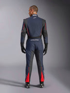 Vue arrière de la combinaison Alpinestars GP Tech V4 en bleu marine, noir et rouge, combinaison de course automobile une pièce avec panneaux extensibles noirs et accents rouges, logo Alpinestars et détails de certification FIA, portée avec gants et bottines de course professionnels.