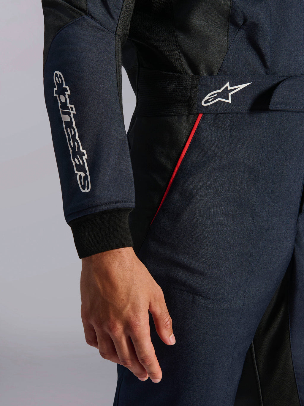 Combinaison Alpinestars GP Tech V4 en bleu marine, noir et rouge, vue détaillée de la taille et de la manche avec logos Alpinestars blancs, liseré rouge et tissu en sergé texturé.