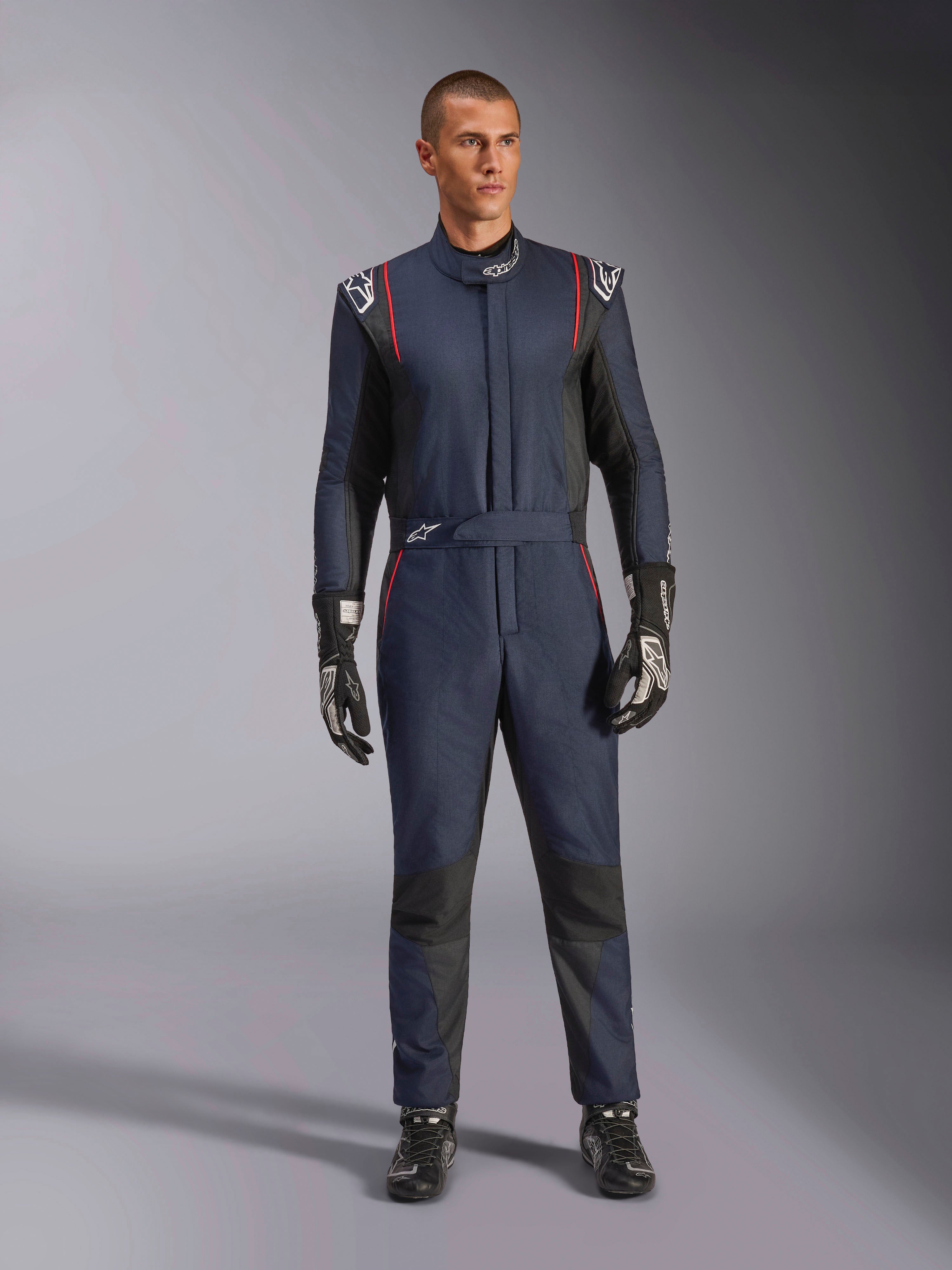 Alpinestars GP Tech V4 Suit, combinaison de course automobile professionnelle bleu marine et noir avec liserés rouges, équipement de course une pièce certifié FIA, portée avec des gants et des chaussures de course noirs, vêtement pour pilote de sport automobile
