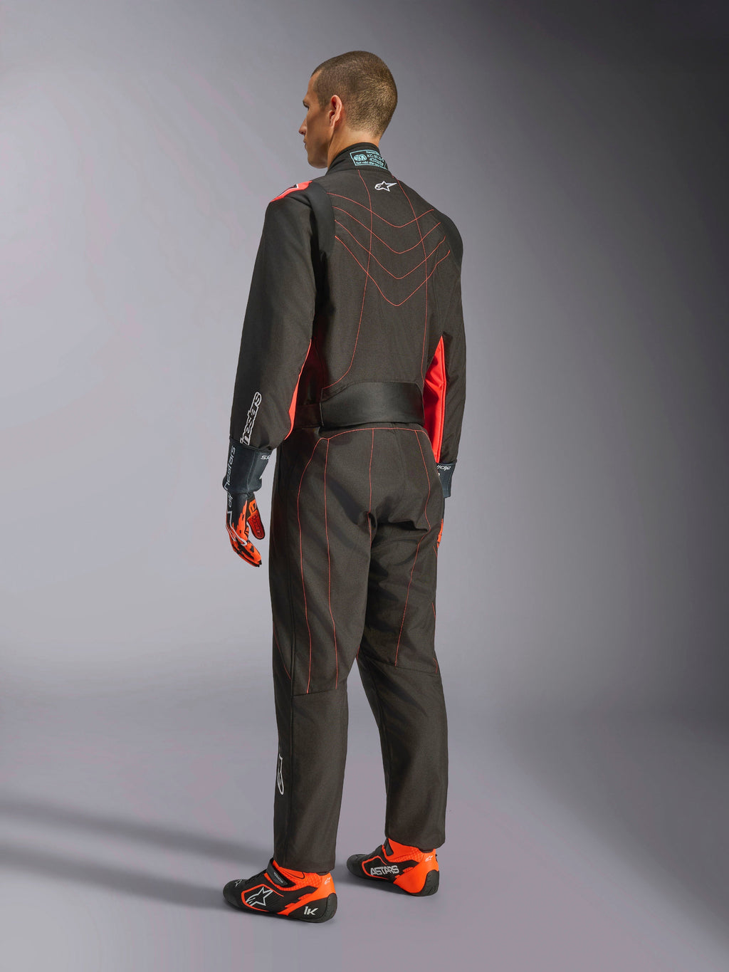 Alpinestars KMX-9 V3 Suit, Karting Race Suit, Black and Red Fluo, back view, featuring red contrast stitching and fluorescent side panels, worn with racing gloves and karting shoes, professional motorsport apparel