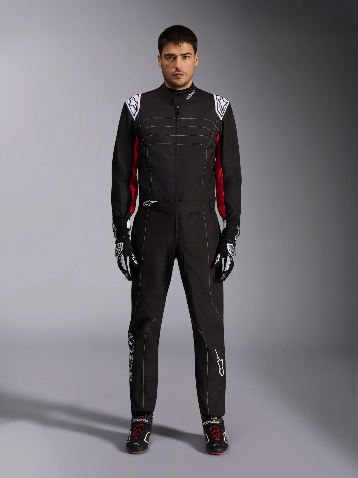 Combinaison de karting Alpinestars KMX-9 V3 en noir, rouge et blanc, vue frontale d'un modèle portant la combinaison une-pièce avec gants et chaussures de course coordonnés, logos Alpinestars blancs sur les épaules et accents rouges.