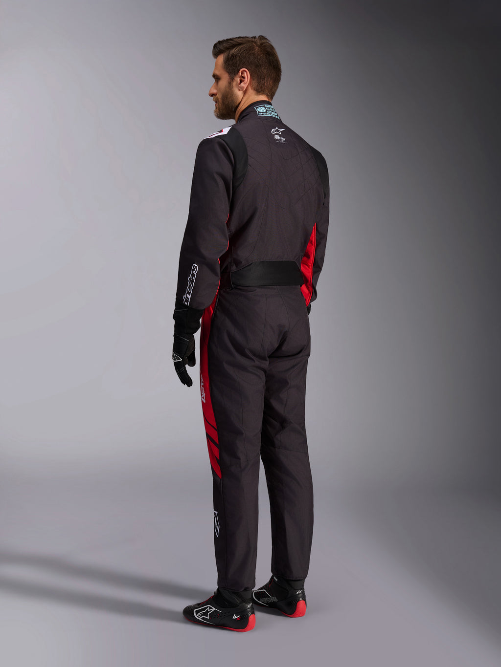 Combinaison Alpinestars KMX-9 V3 Graphic 3, noir et rouge, vue arrière d'un mannequin portant un équipement complet de karting comprenant des gants noirs et des bottes de course, avec des panneaux latéraux rouges et des détails de logos blancs.