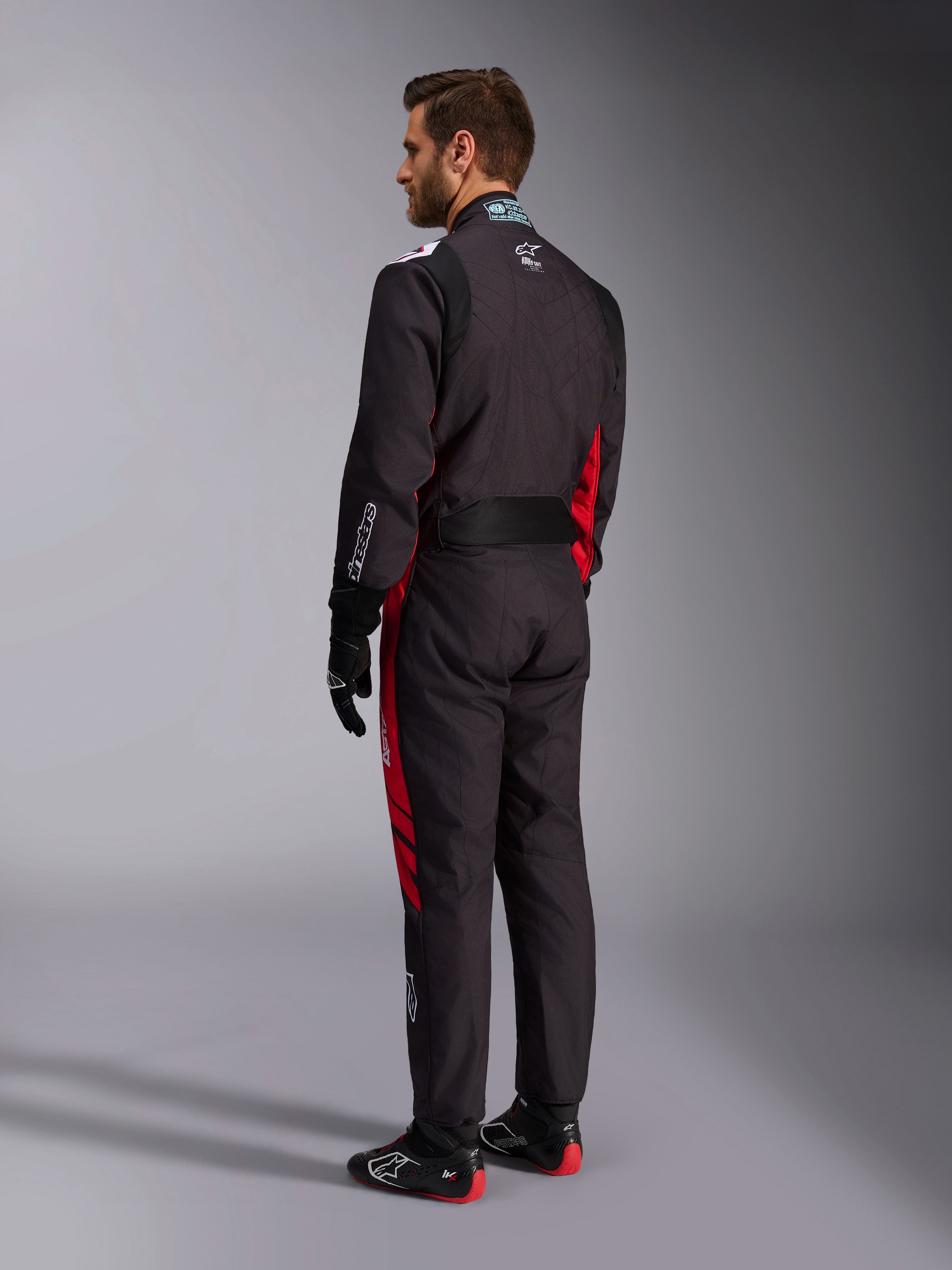 Combinaison Alpinestars KMX-9 V3 Graphic 3, noir et rouge, vue arrière d'un mannequin portant un équipement complet de karting comprenant des gants noirs et des bottes de course, avec des panneaux latéraux rouges et des détails de logos blancs.