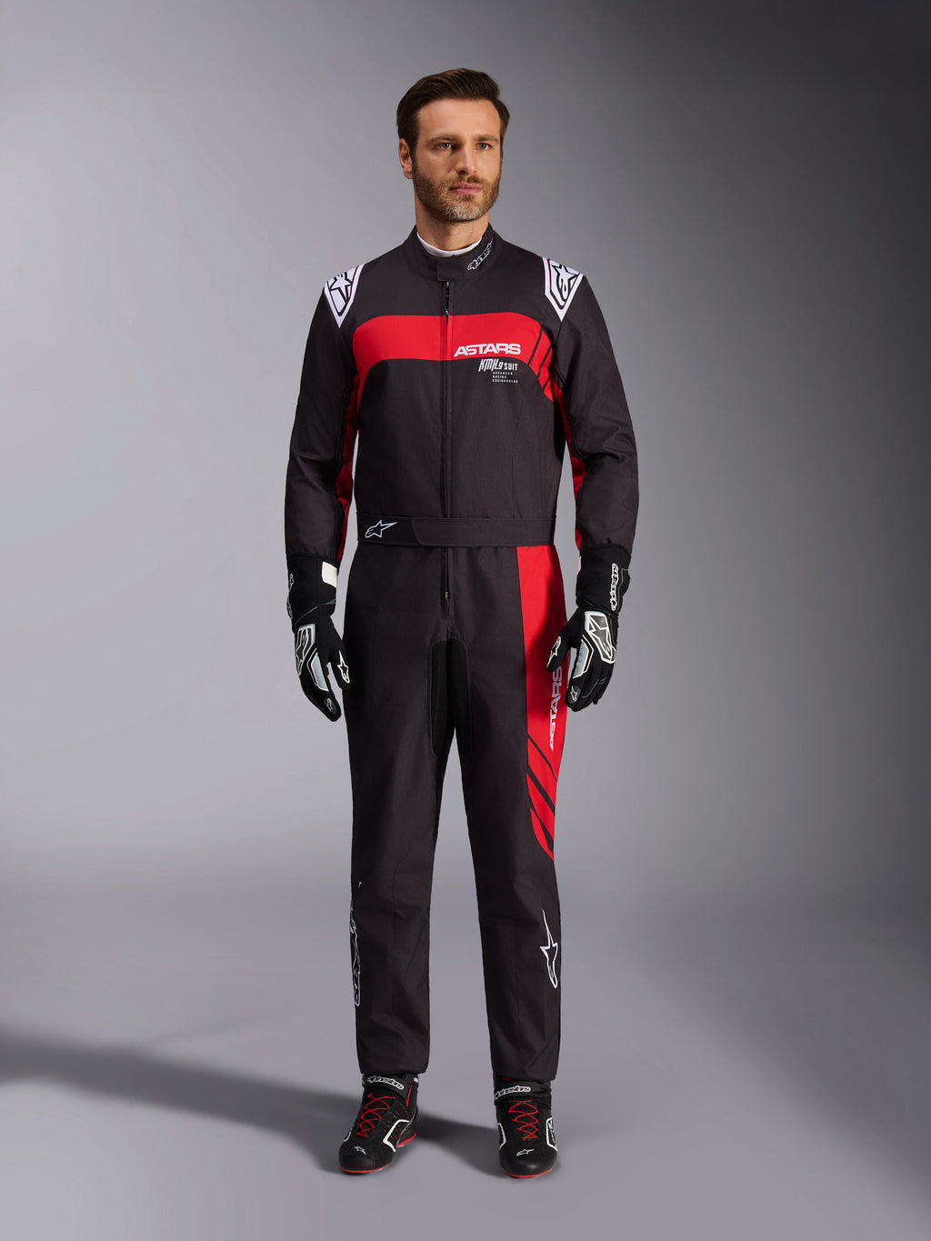 Combinaison Alpinestars KMX-9 V3 Graphic 3, combinaison de karting, noir et rouge, vue frontale en pied portée par un mannequin, avec des empiècements graphiques rouges et des logos blancs, associée à des gants et des chaussures de course noirs, équipement de sport automobile professionnel.