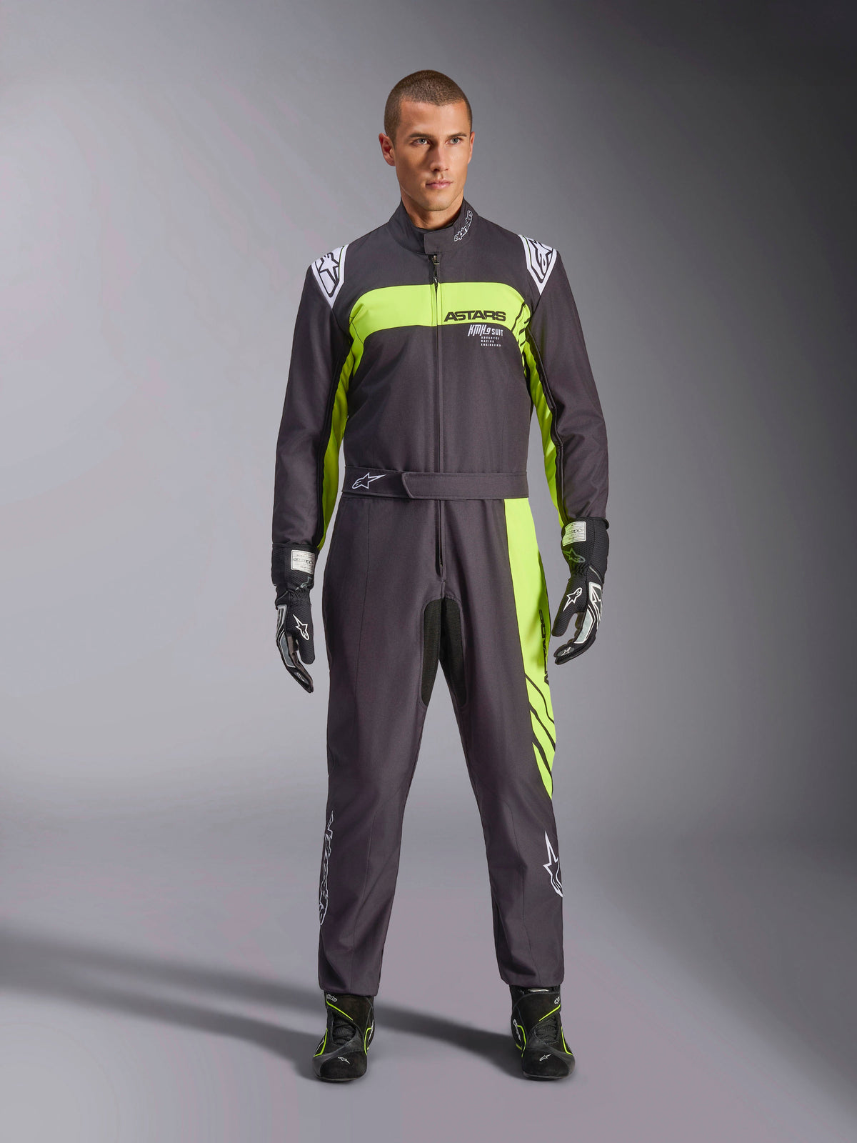 Combinaison Alpinestars KMX-9 V3 Graphic 3, noir et jaune fluo, combinaison de karting monopièce professionnelle portée par un mannequin, présentant des accents jaune fluo vifs, le logo ASTARS sur la poitrine, avec gants et bottes de course assortis.