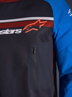 Maillot Alpinestars Maxdura Dual, gros plan sur la poitrine et la manche, gris foncé et bleu royal, avec poche poitrine zippée, torse en maille respirante et rembourrage intégré sur les manches, logo Alpinestars sur bandes rouges et blanches