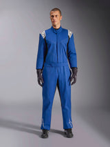Modèle masculin portant la combinaison Alpinestars Kart Indoor V2 en bleu, combinaison de karting une pièce avec logos étoiles blancs sur les épaules et les tibias, coutures contrastées blanches, ceinture élastique à la taille, assortie à des gants et des chaussures de course noirs, conçue pour une utilisation récréative sur piste