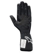 Gants Alpinestars Tech-1 Race V4, gants de course automobile professionnels, noir tar gray, vue côté paume avec motifs d'adhérence en silicone étendus sur les doigts et la paume, manchette étendue avec logo Alpinestars blanc et étiquettes d'homologation FIA/SFI