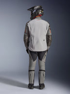 Veste Alpinestars Nazca 3L GORE-TEX PRO, veste de moto d'aventure, gris foncé et gris moyen, vue arrière d'un motard portant l'équipement complet, portée avec un pantalon assorti et un casque d'aventure noir, avec un logo rouge au dos et des renforts en Superfabric aux coudes, conception textile durable pour le touring d'aventure.