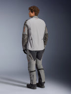 Veste Alpinestars Nazca 3L GORE-TEX PRO, veste de moto d'aventure, gris foncé et gris moyen, vue arrière portée avec un pantalon d'aventure assorti et des bottes noires, avec des renforts Superfabric gris foncé sur les manches, des touches orange sur les fermetures éclair et un petit logo rouge au col arrière.