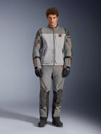 Veste Alpinestars Nazca 3L GORE-TEX PRO, veste de moto adventure, gris foncé et gris moyen, portée par un mannequin avec pantalon assorti et gants noirs, avec des accents orange sur les fermetures éclair et un logo rouge sur la poitrine, équipement de protection technique pour la conduite extrême