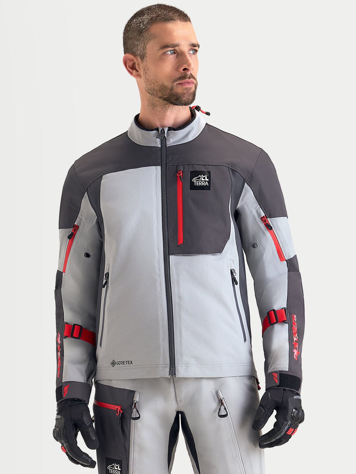 Alpinestars Arenis Gore Tex Veste, veste de moto adventure pour homme en gris moyen, gris foncé et noir, vue de face portée par un modèle mettant en valeur la construction textile imperméable et la poche de poitrine zippée
