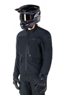 Veste Alpinestars St-7 Prime GORE-TEX, veste de moto noire, portée par un pilote avec un casque noir et des lunettes de protection, dotée de grandes poches cargo sur la poitrine et d'une coque imperméable laminée, équipement premium pour l'aventure touring et les trajets quotidiens.