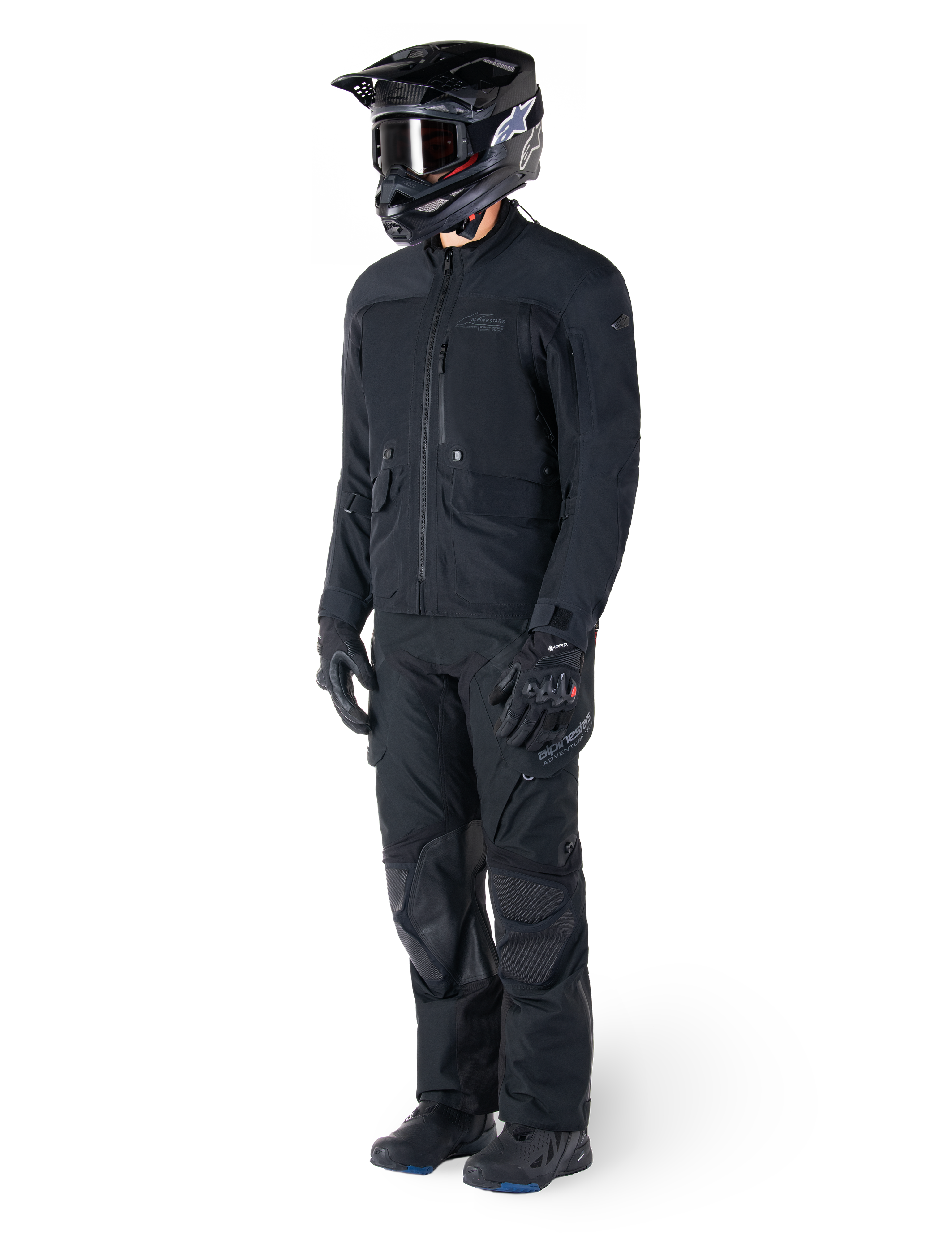 Motocycliste portant la veste Alpinestars St-7 Prime GORE-TEX noire, tenue d'aventure touring coordonnée avec pantalon noir assorti, casque noir avec lunettes et gants, présentant un design épuré et fonctionnel pour des performances par tous les temps.