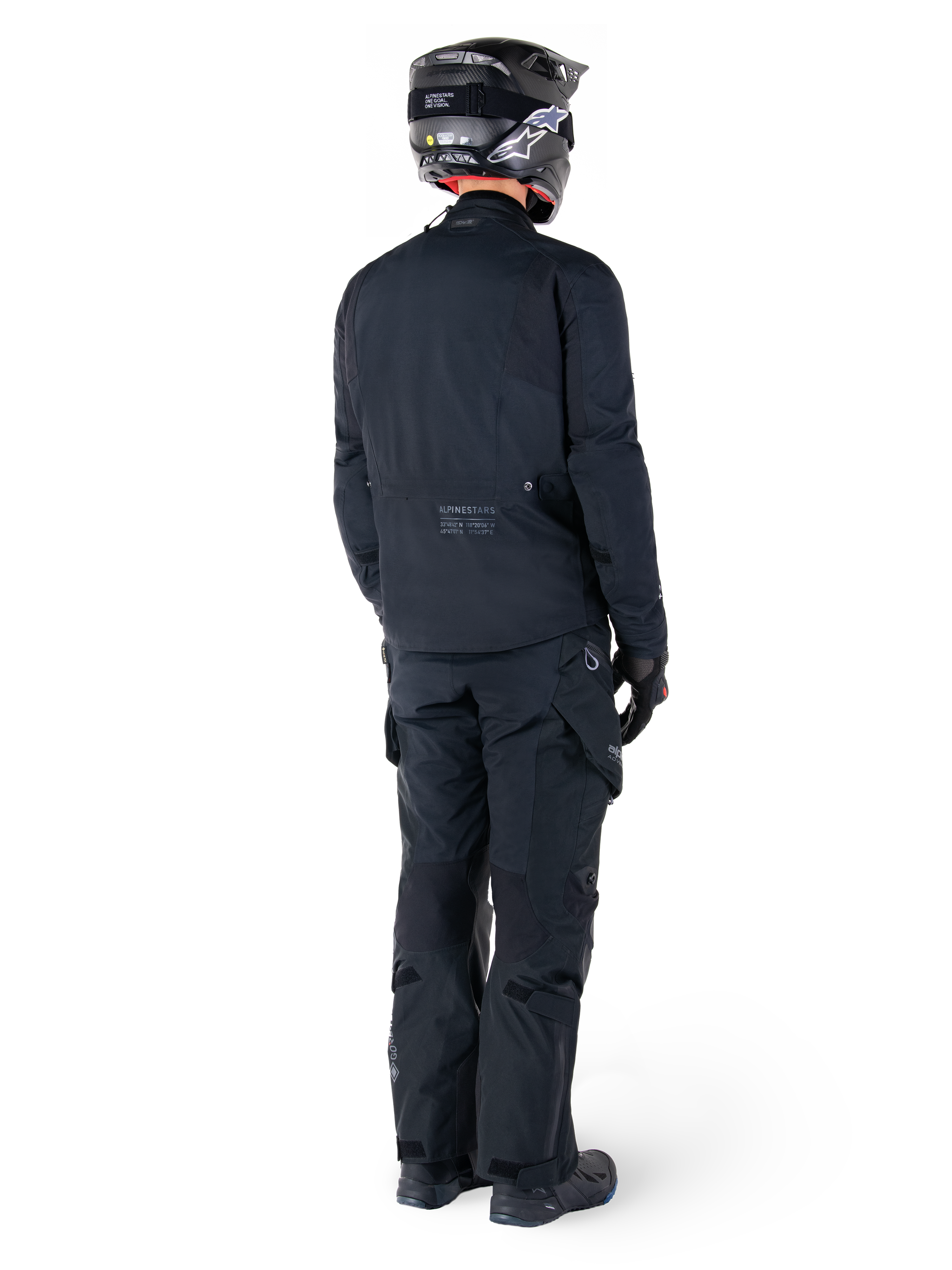 Vue arrière d'un pilote portant la veste Alpinestars St-7 Prime GORE-TEX noire, associée à un pantalon de touring noir assorti, un casque de moto noir avec logo blanc et des bottes de moto noires, équipement d'aventure protecteur complet pour le touring et les trajets quotidiens.