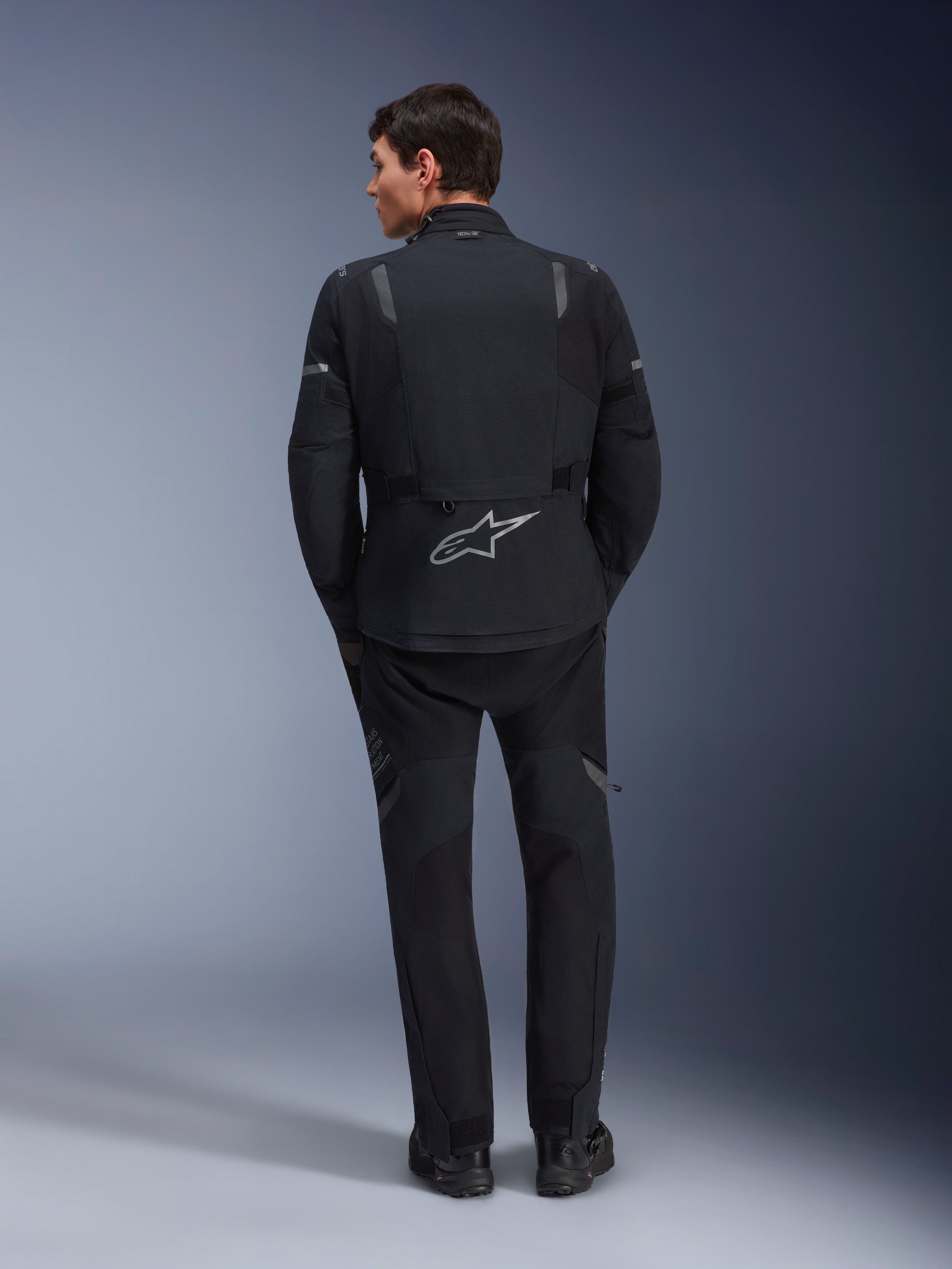 Veste Alpinestars ST-7 2L GORE-TEX et pantalon ST-7 2L GORE-TEX assorti, équipement de moto d'aventure noir et gris foncé, vue arrière montrant le logo Alpinestars réfléchissant sur la veste et la construction textile technique.