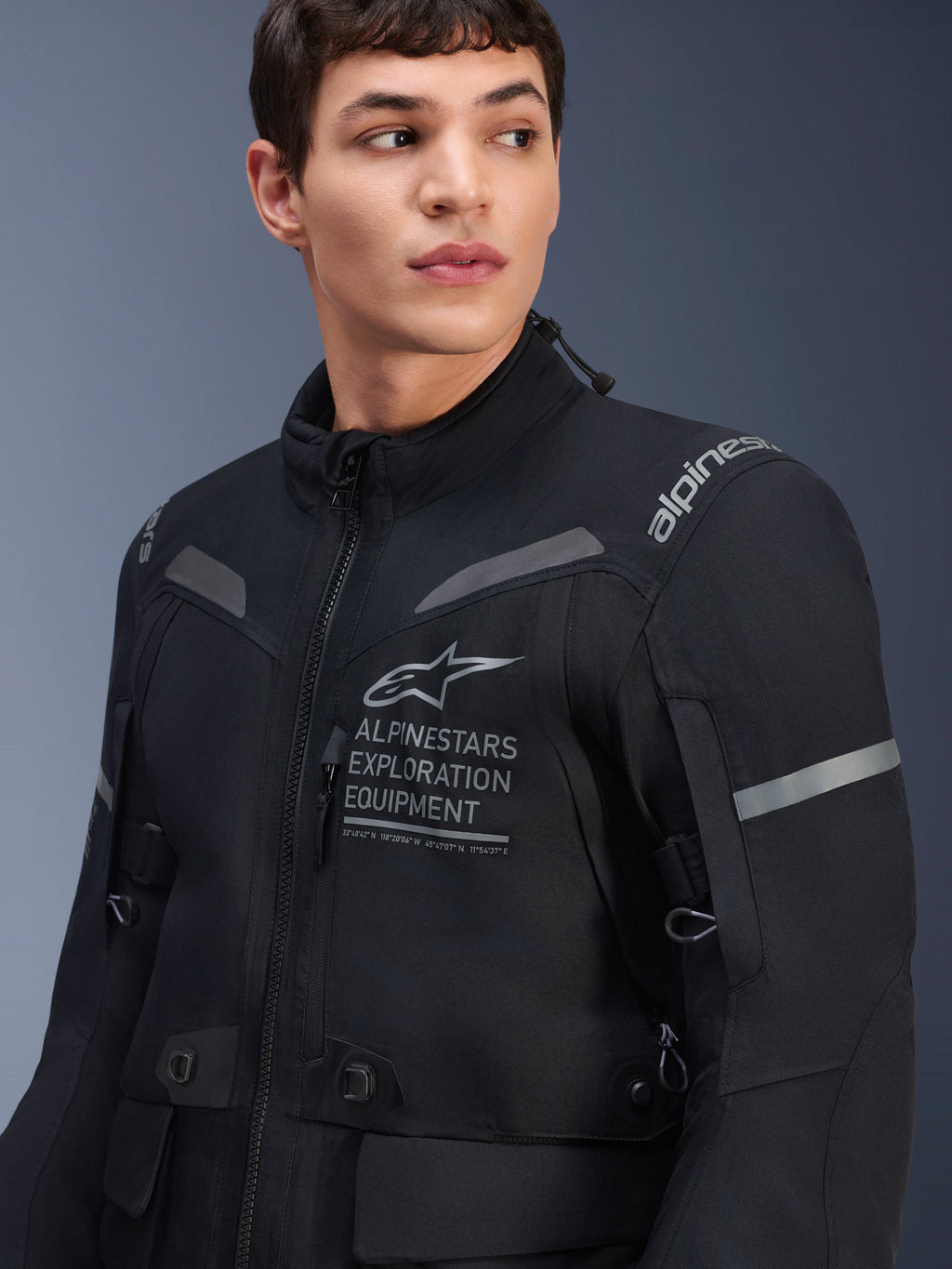 Veste Alpinestars ST-7 2L GORE-TEX, veste de moto, noir et gris foncé, portée par un mannequin homme, avec logo Alpinestars Exploration Equipment sur la poitrine, accents gris réfléchissants et construction textile prête pour l'aventure
