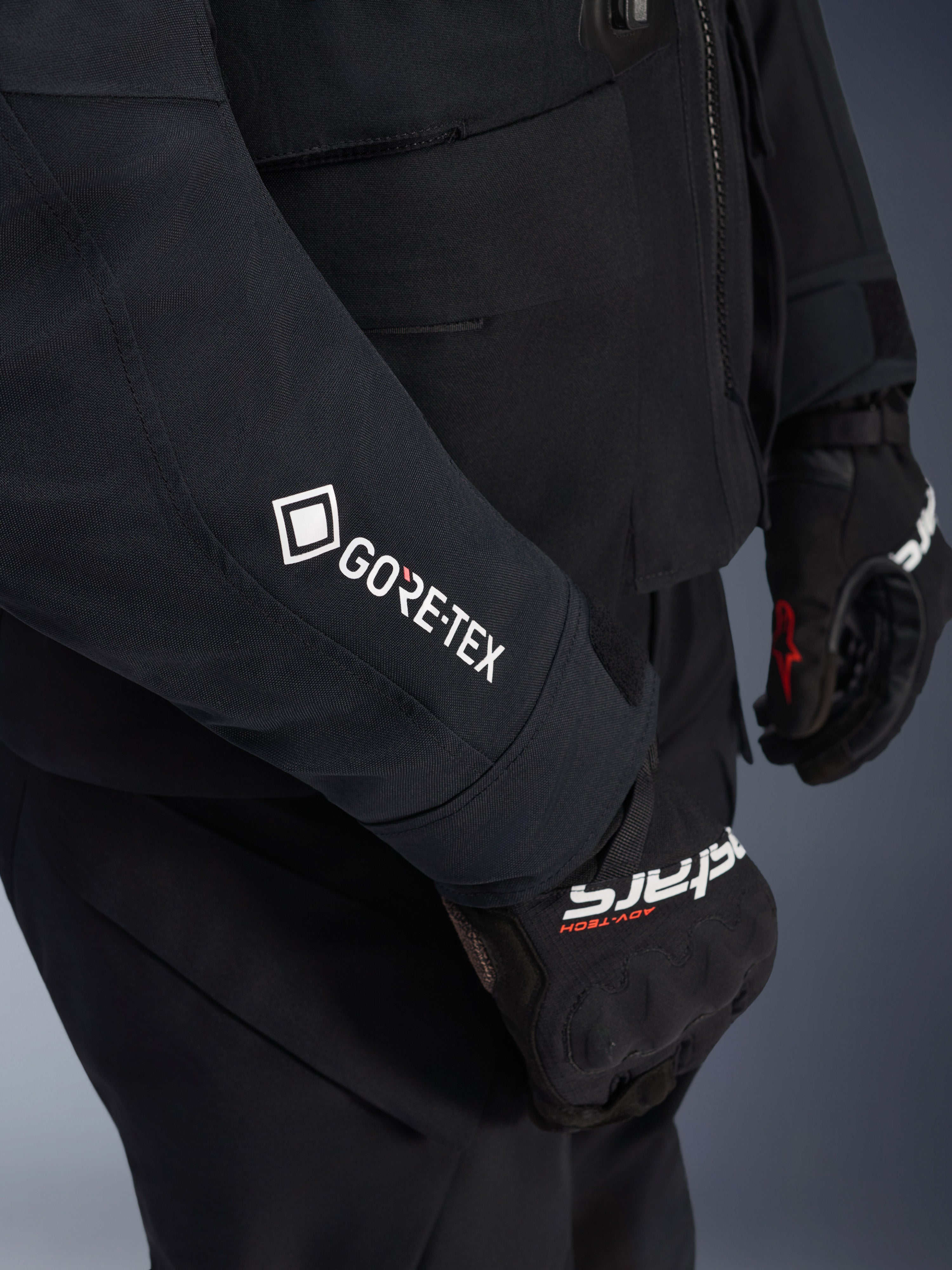 Veste Alpinestars ST-7 2L GORE-TEX, noir et gris foncé, gros plan sur la manche avec marquage GORE-TEX blanc, portée avec des gants de moto adventure noirs, vêtement de moto imperméable