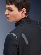 Veste Alpinestars ST-7 2L GORE-TEX, veste de moto noire et gris foncé, vue rapprochée du col montrant l'ajustement par cordon de serrage et l'étiquette Tech-Air, avec accents réfléchissants gris et logo de la marque sur l'épaule.