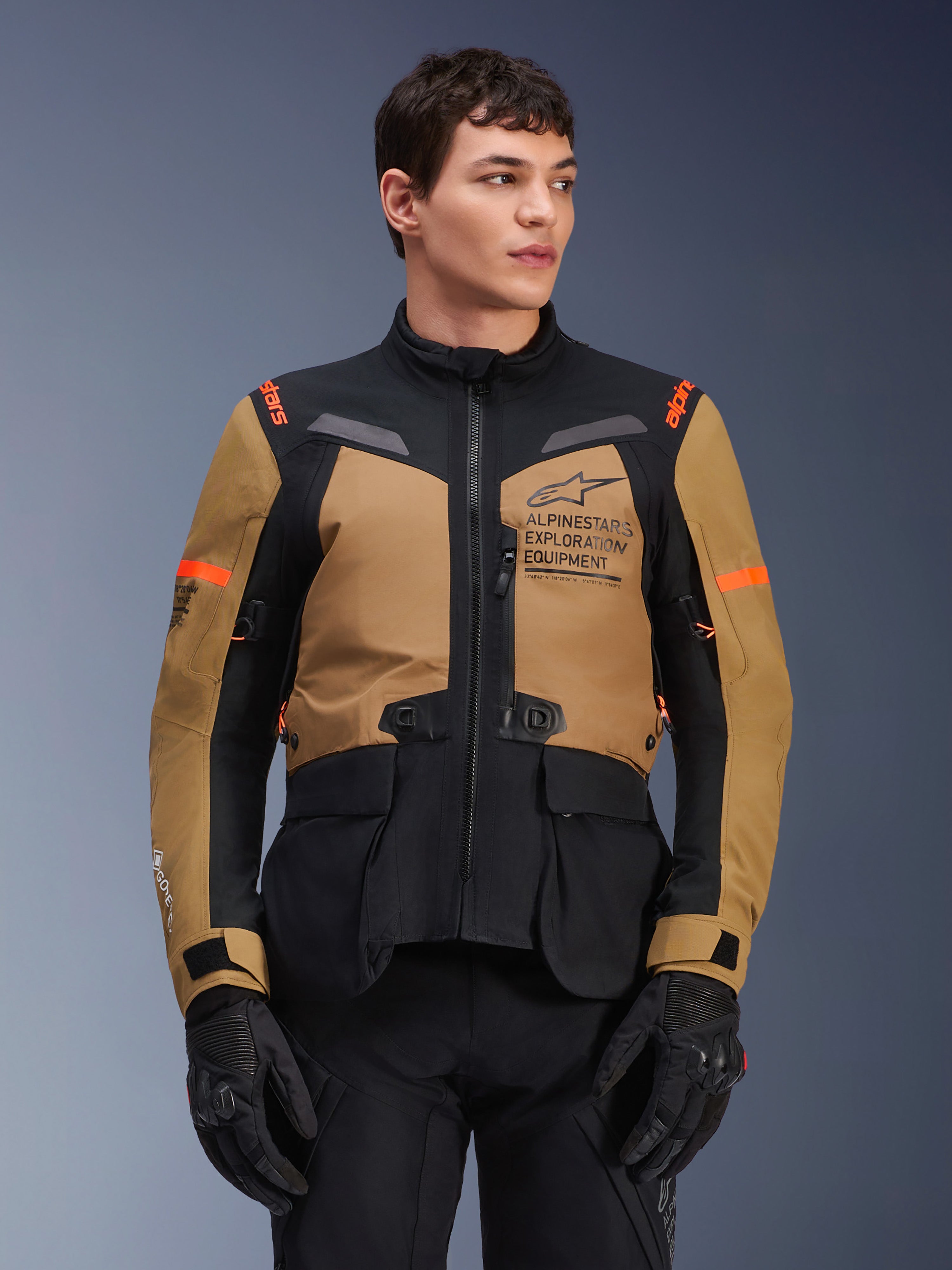 Veste Alpinestars ST-7 2L GORE-TEX, veste de moto touring aventure, marron Gobi et noir avec accents orange, portée par un mannequin homme, logo Exploration Equipment et technologie GORE-TEX, équipement imperméable et résistant