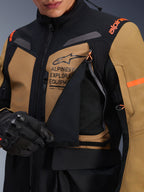 Veste Alpinestars ST-7 2L GORE-TEX, veste de moto d'aventure touring, brun Gobi et noir, gros plan montrant le panneau de ventilation de la poitrine ouvert révélant une maille respirante, avec le logo Alpinestars Exploration Equipment et des touches d'orange.