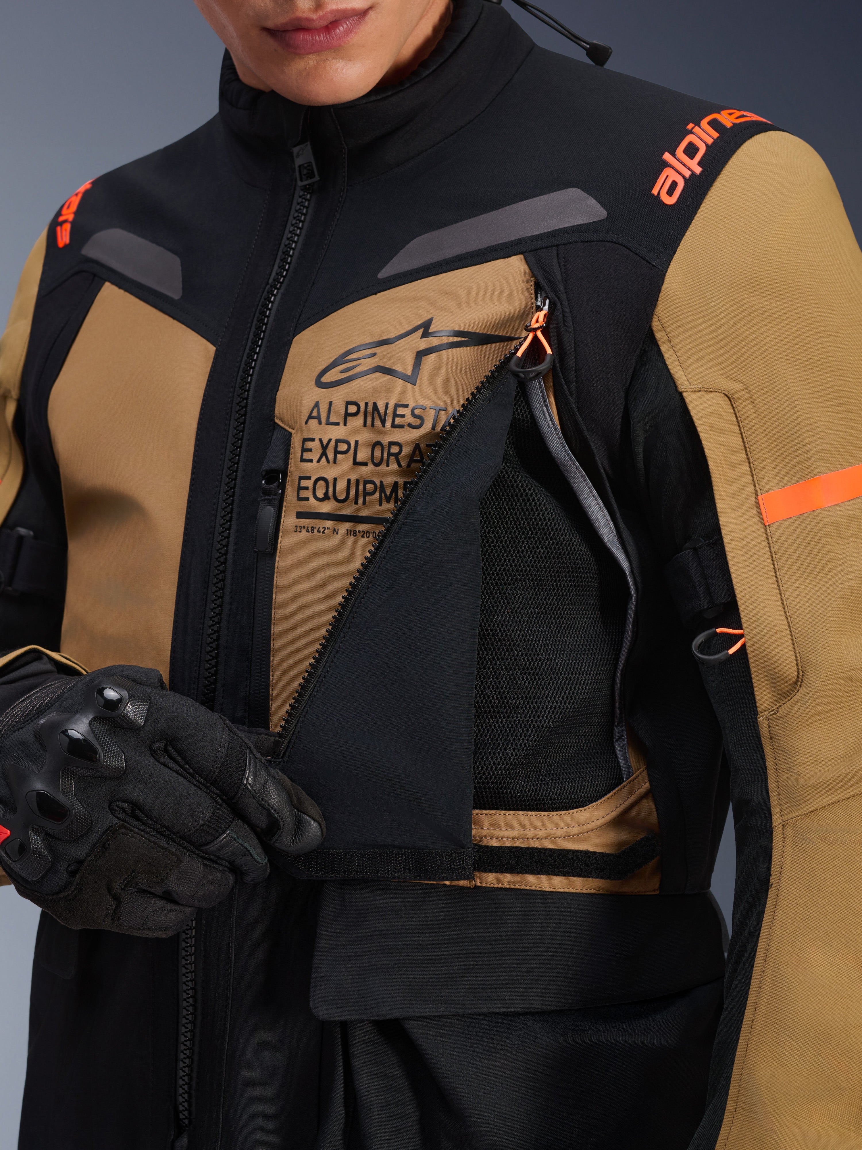 Veste Alpinestars ST-7 2L GORE-TEX, veste de moto d'aventure touring, brun Gobi et noir, gros plan montrant le panneau de ventilation de la poitrine ouvert révélant une maille respirante, avec le logo Alpinestars Exploration Equipment et des touches d'orange.