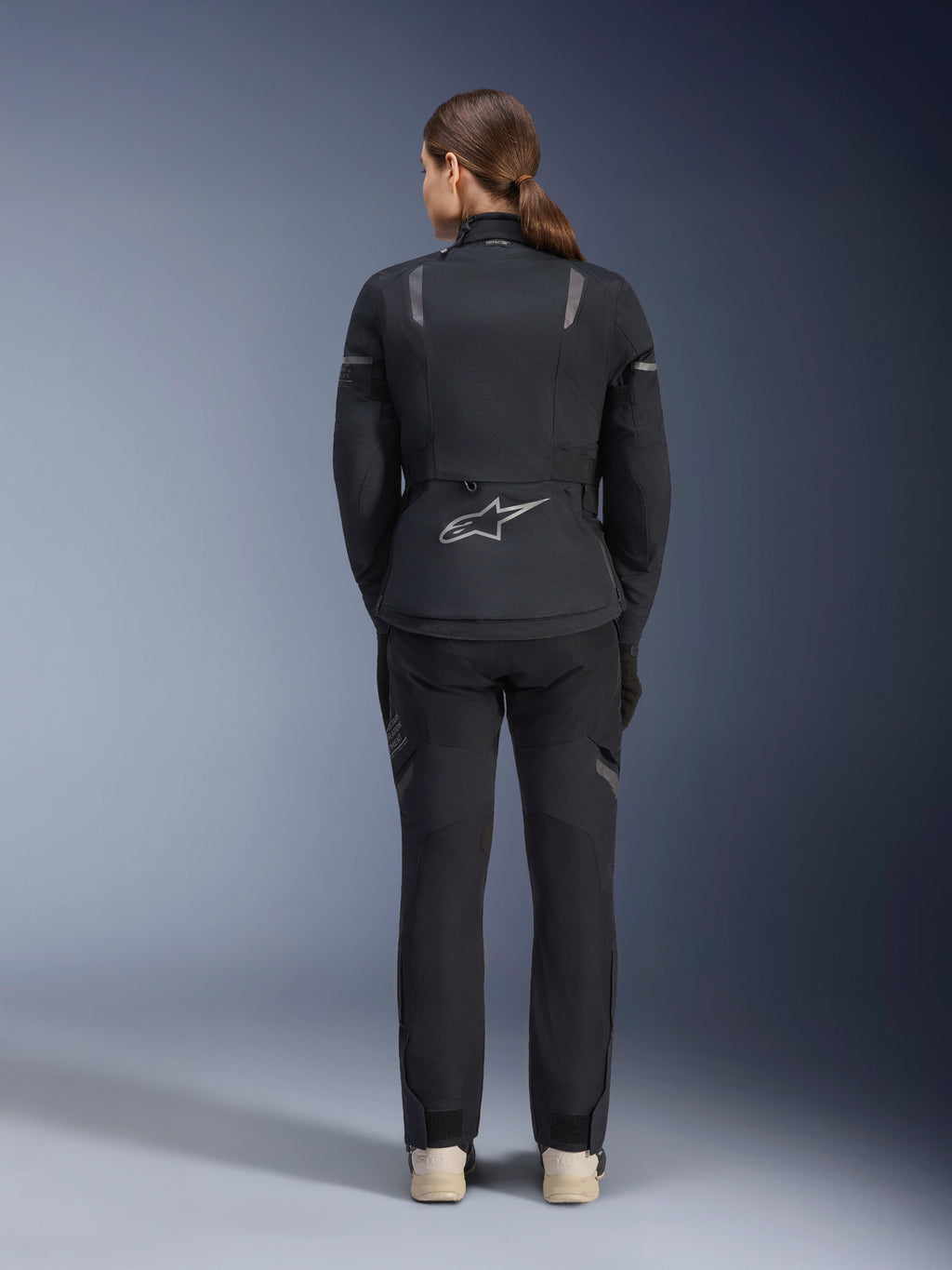 Veste Alpinestars Stella ST-7 2L GORE-TEX pour femme, noir et gris foncé, vue de dos montrant le logo Alpinestars argenté au bas du dos, associée à un pantalon textile noir assorti, équipement de moto adventure touring