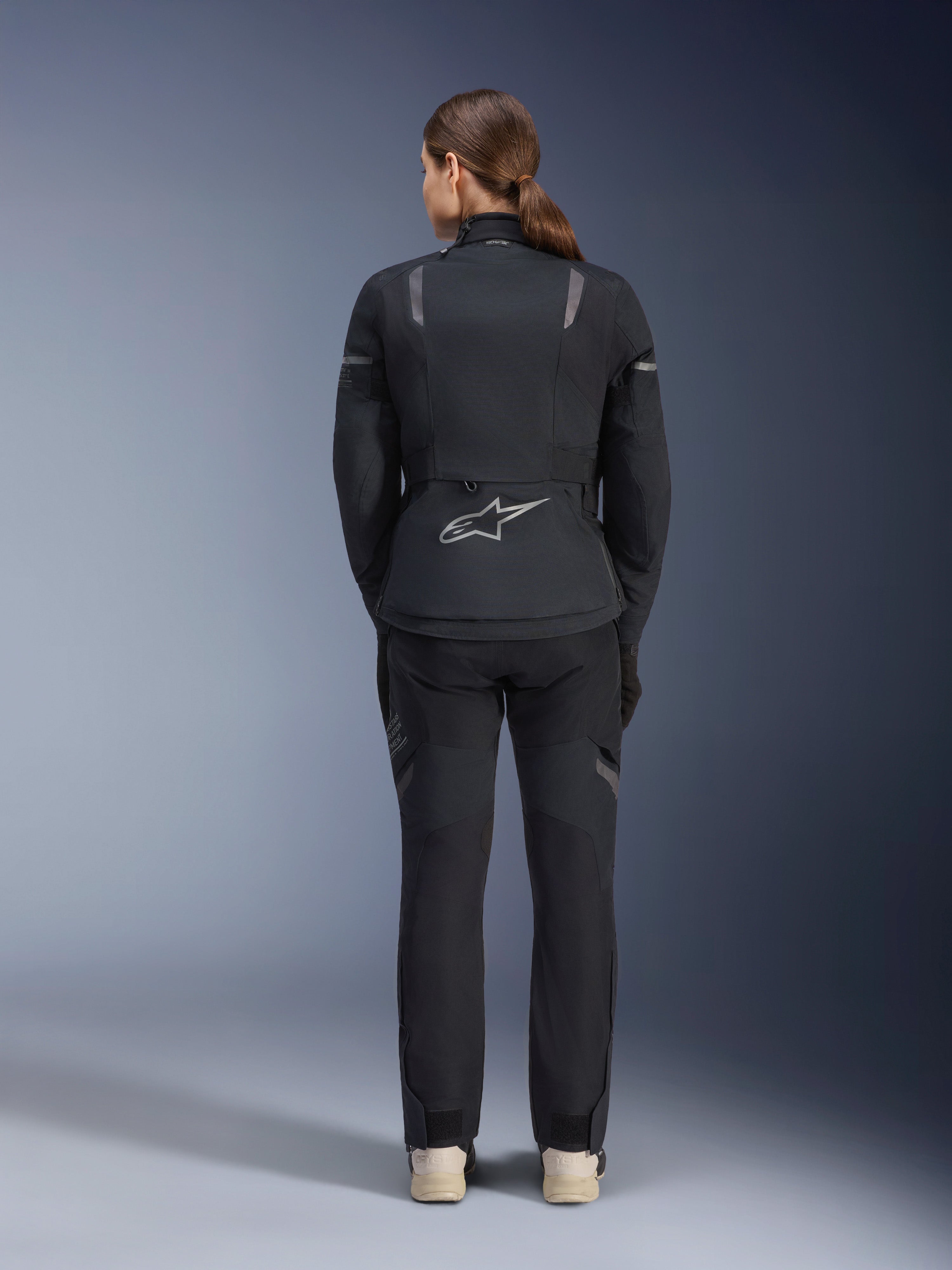Veste Alpinestars Stella ST-7 2L GORE-TEX pour femme, noir et gris foncé, vue de dos montrant le logo Alpinestars argenté au bas du dos, associée à un pantalon textile noir assorti, équipement de moto adventure touring