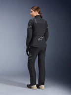 Veste Stella ST-7 2L GORE-TEX pour femme, noir et gris foncé, veste de touring aventure vue de dos, portée avec un pantalon noir assorti et des bottes crème, arborant le logo Alpinestars sur le bas du dos, conçue pour le touring routier toutes saisons