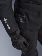 Veste Alpinestars Stella ST-7 2L GORE-TEX pour femme, veste de touring aventure noire, vue rapprochée de la manche avec le logo GORE-TEX blanc, texte « Alpinestars Exploration Equipment » sur la hanche, gant de moto noir, matériau textile imperméable avec poches cargo fonctionnelles