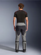 Pantalon Alpinestars Nazca 3L GORE-TEX PRO, pantalon de moto d'aventure gris foncé et noir, vue arrière sur un modèle, design technique multi-panneaux en tissu gris et noir, avec ajusteurs de volume aux mollets, porté avec une sous-couche noire aux accents rouges