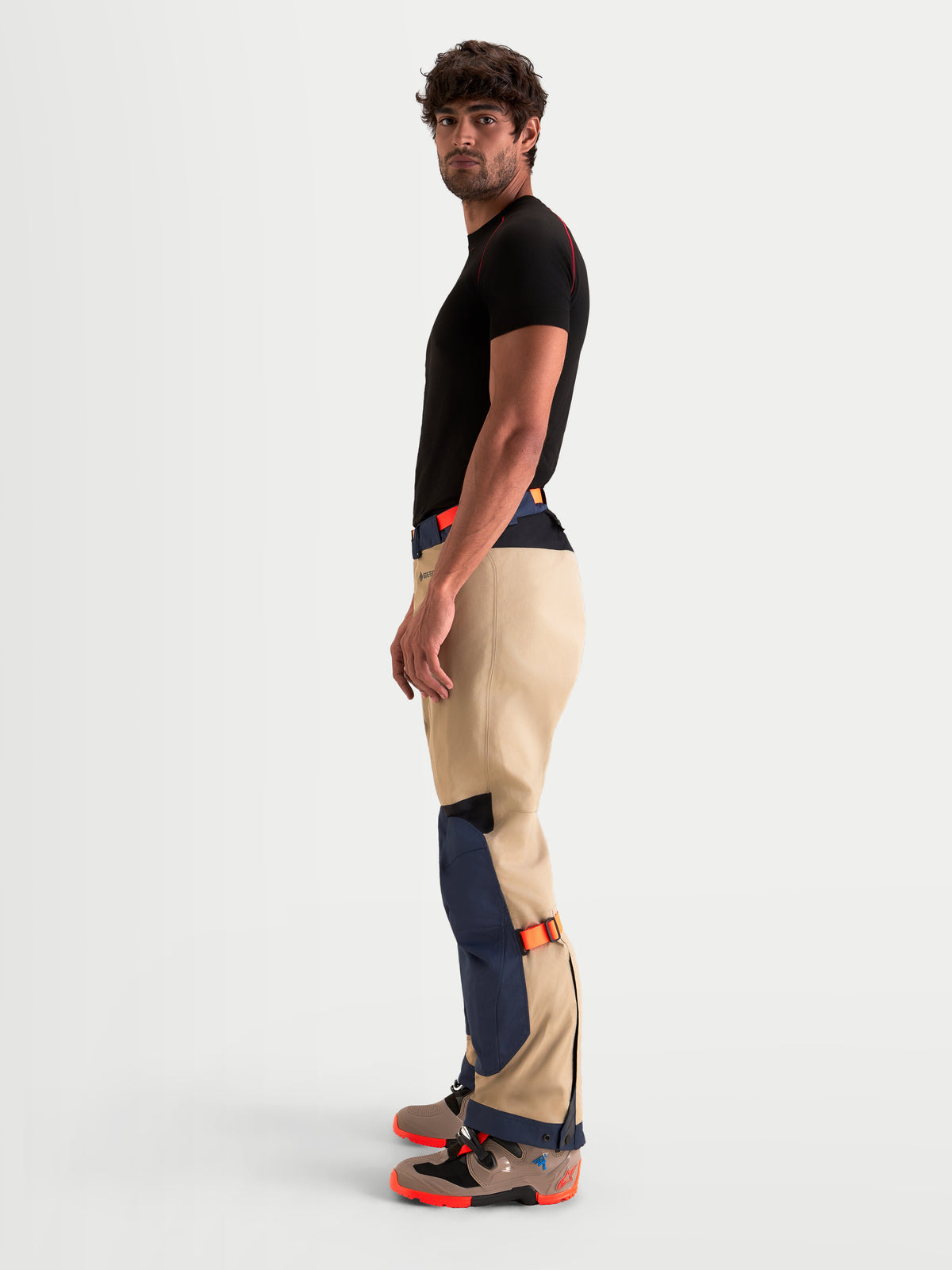 Alpinestars Arenis Gore-Tex Pantalons, pantalon de moto adventure pour homme en bleu marine et aluminium, vue de profil par un modèle mettant en valeur la construction imperméable en textile et les dispositifs de réglage sur le bas de la jambe