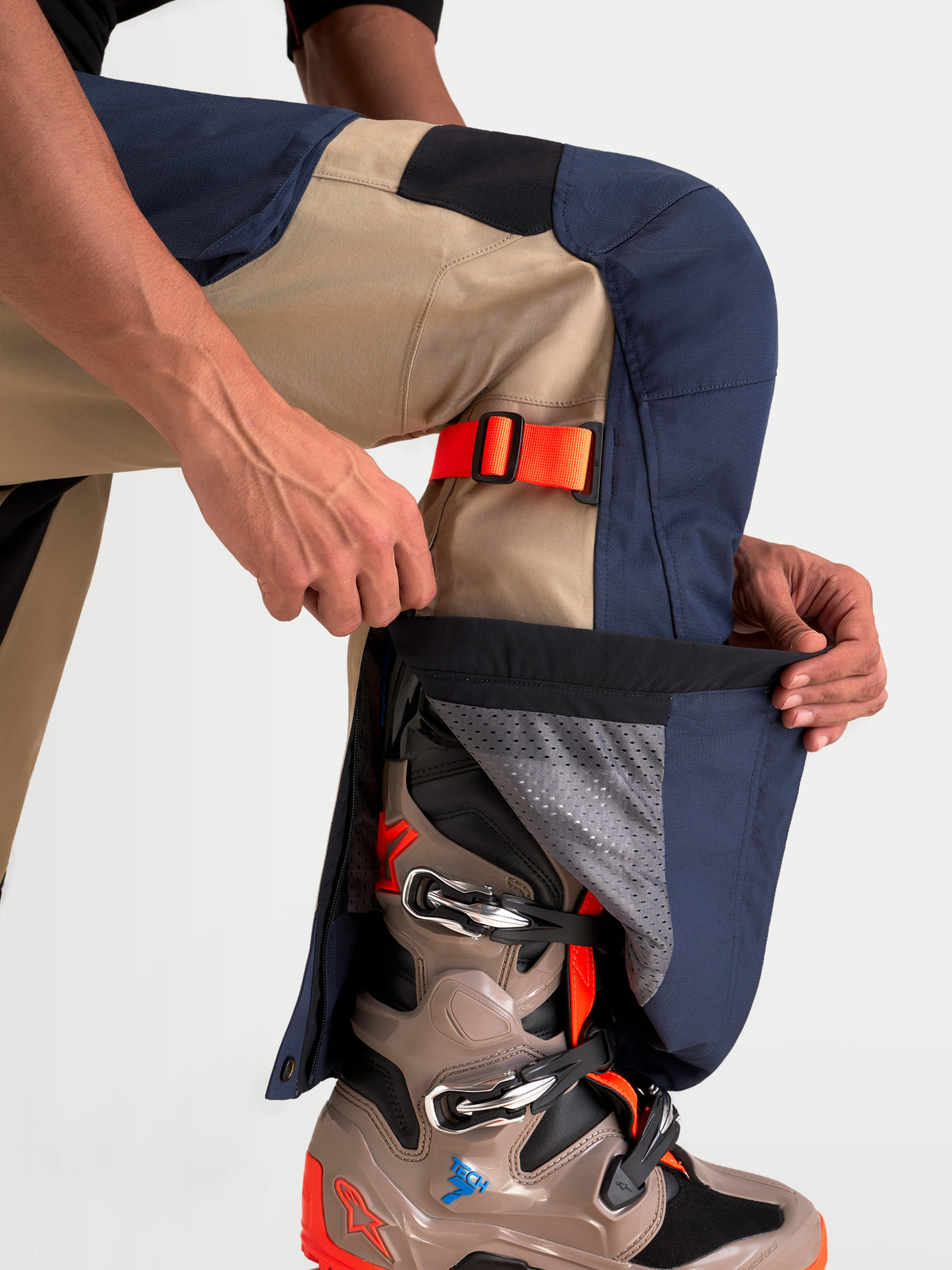 Alpinestars Arenis Gore-Tex Pantalons, pantalon de moto adventure pour homme bleu marine et aluminium, vue rapprochée d'un pilote ajustant la fermeture éclair du bas de jambe sur une botte adventure, construction en textile imperméable