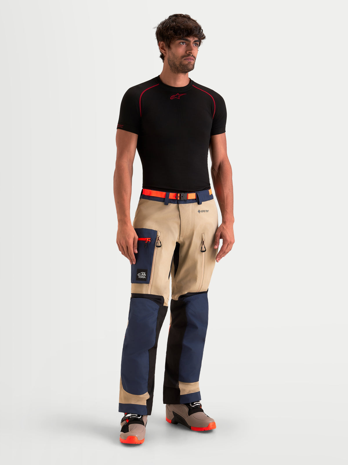 Alpinestars Arenis Gore-Tex Pantalons, pantalon de moto adventure pour homme bleu marine, beige et noir, vue de face porté par un modèle avec un t-shirt noir, doté d'une construction imperméable GORE-TEX et d'une poche cargo