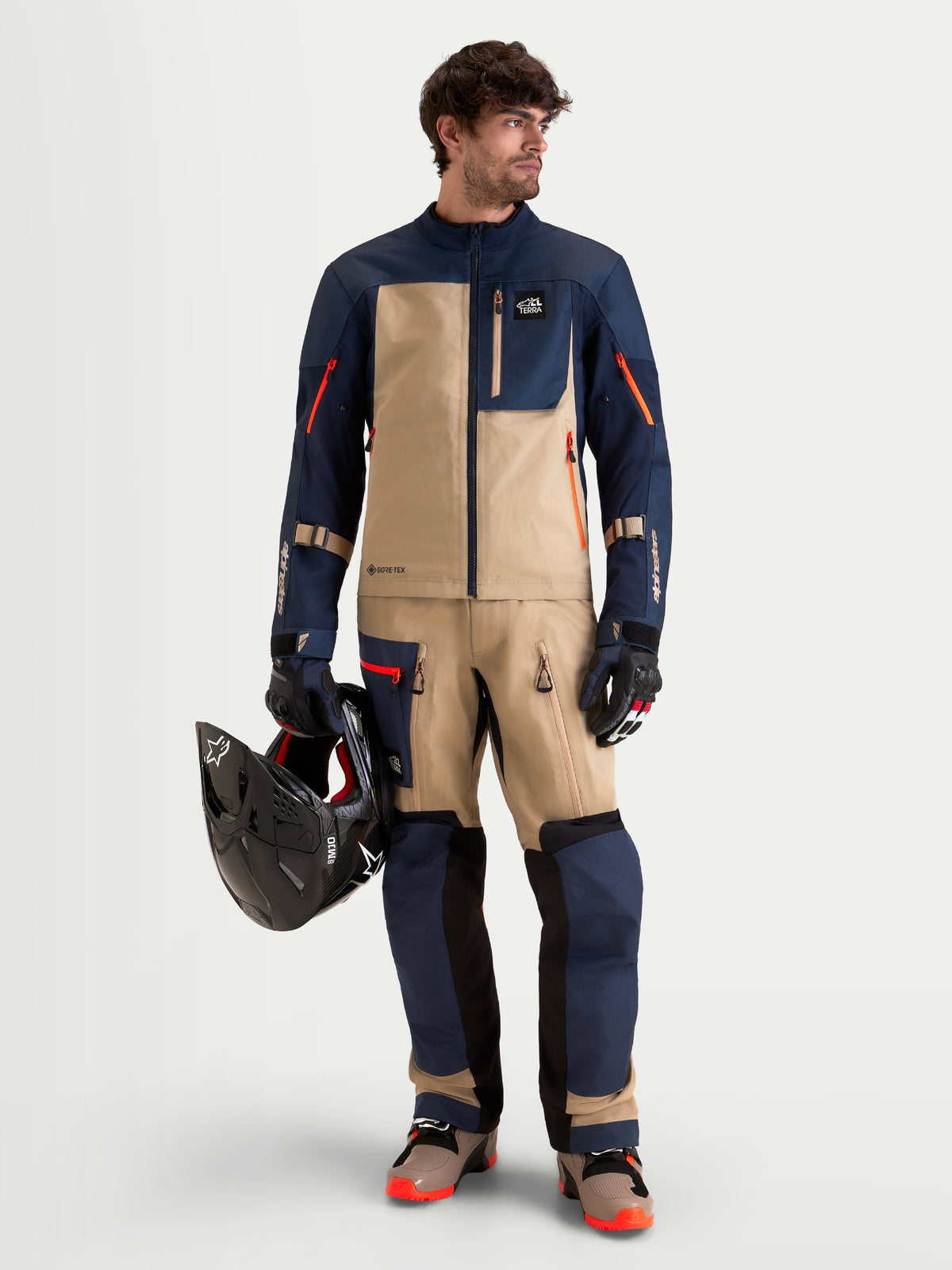 Alpinestars Arenis Gore-Tex Pantalons, pantalon de moto adventure pour homme en bleu nuit et aluminium, porté par un modèle tenant un casque comme partie de l'équipement ADV assorti