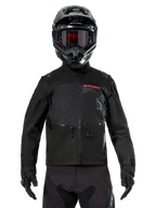 Veste Alpinestars Pro-Dura, veste de moto tout-terrain noire, vue de face portée par un pilote avec un casque et des lunettes noirs assortis, logo Alpinestars rouge, poches de poitrine zippées et construction textile durable pour l'enduro.