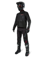 Pilote de motocross portant un équipement de course complet, veste Alpinestars Pro-Dura noire, pantalon noir avec marquage gris et accents rouges, casque noir avec lunettes, et bottes de motocross noires et blanches, tenue coordonnée pour l'enduro et le tout-terrain