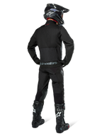Veste Alpinestars Pro-Dura, veste d'enduro tout-terrain noire, vue arrière portée avec le pantalon assorti et des bottes Tech 10 noires, logo Alpinestars distinctif dans le bas du dos, construction en textile robuste pour une conduite agressive sur sentier