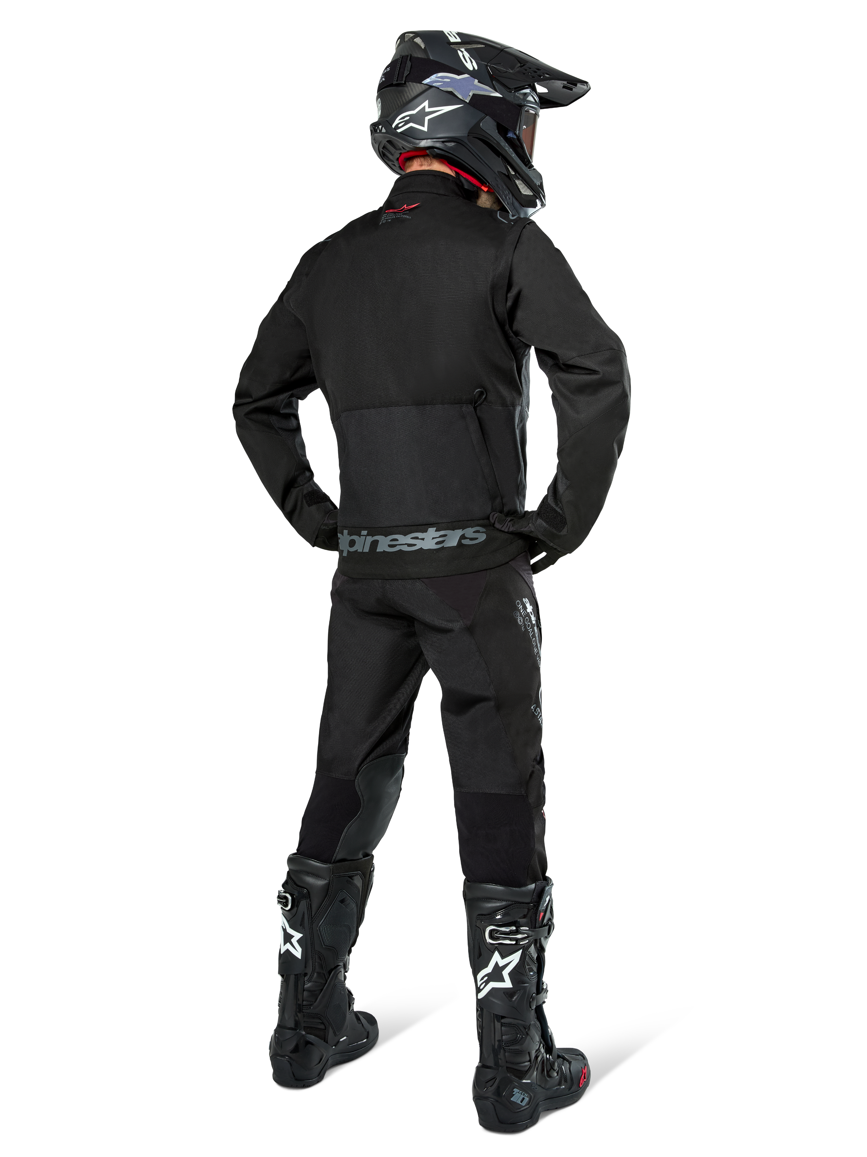 Veste Alpinestars Pro-Dura, veste d'enduro tout-terrain noire, vue arrière portée avec le pantalon assorti et des bottes Tech 10 noires, logo Alpinestars distinctif dans le bas du dos, construction en textile robuste pour une conduite agressive sur sentier