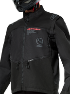 Veste Alpinestars Pro-Dura, veste de moto tout-terrain noire avec marquage Alpinestars rouge et logo Astars circulaire gris sur la poitrine, poches zippées et construction en textile ripstop robuste, design inspiré du rallye pour la pratique de l'enduro.